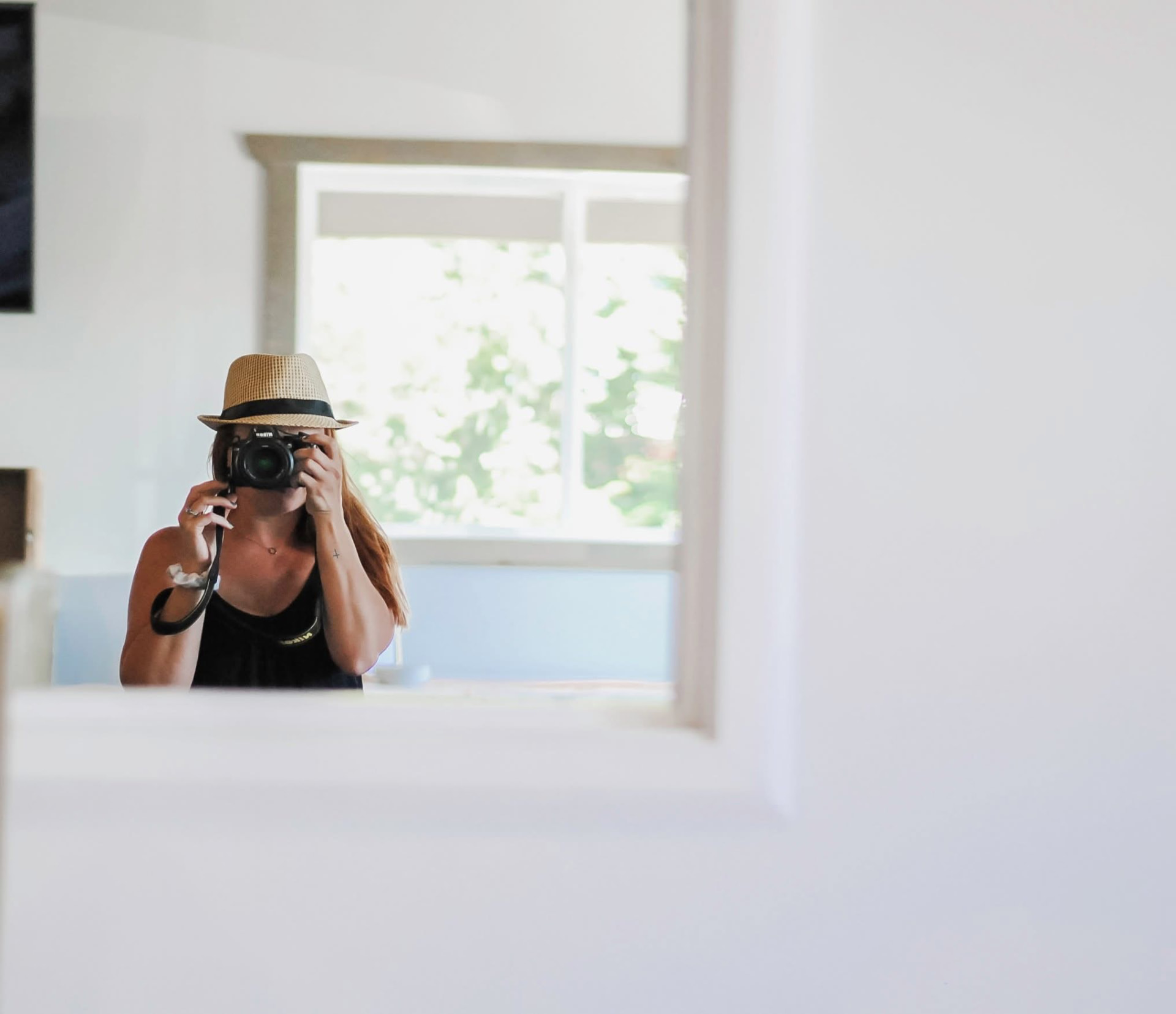 Jessica Faber in a straw hat photographing her reflection in a sunlit mirror