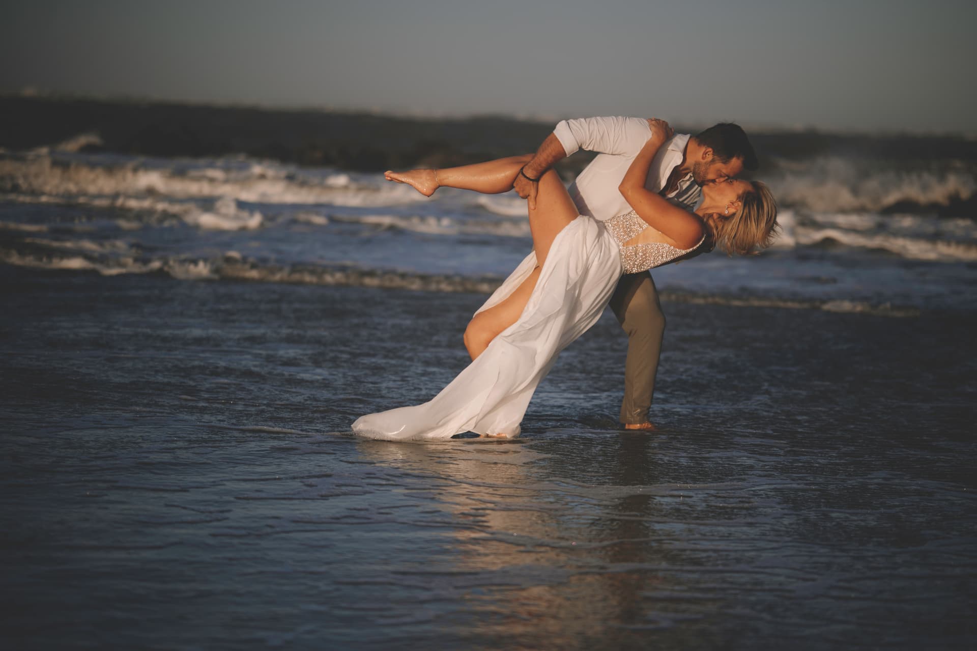 Lowcountry engagement photographer — couple sharing a dramatic dip and kiss in the ocean surf at sunset
