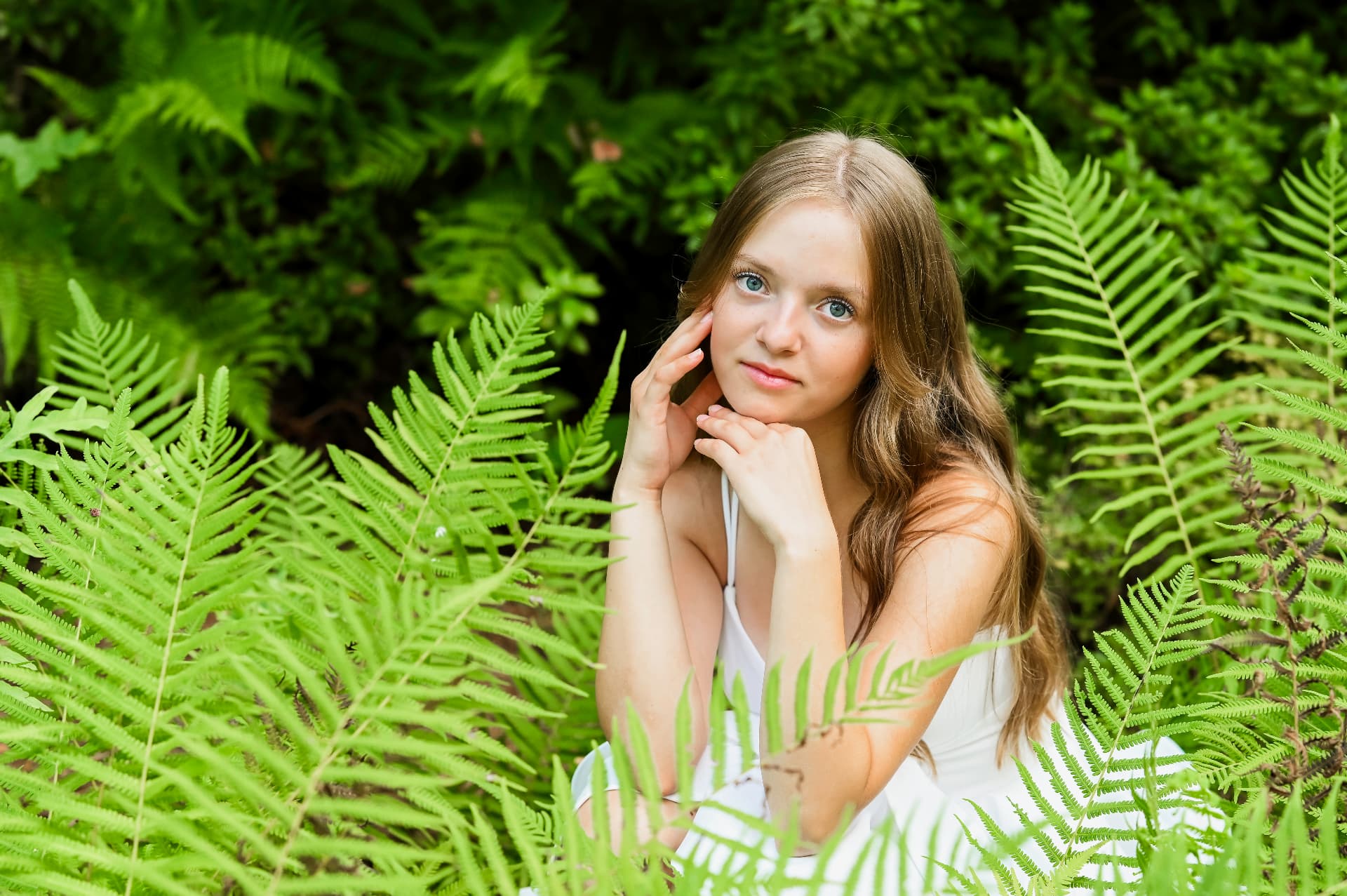 Charleston senior photographer — senior girl in a white dress resting her chin on her hands among lush green ferns