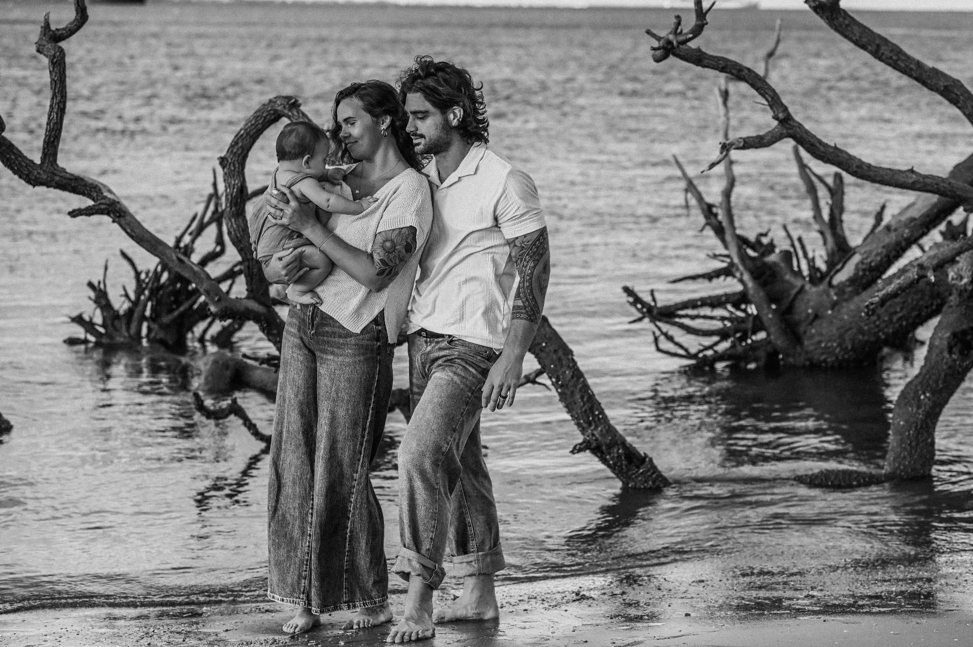 Charleston family photographer — black and white photo of parents holding their baby among driftwood trees on a Lowcountry beach